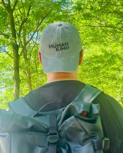 Person wearing a Human Kind cap walking through woodland